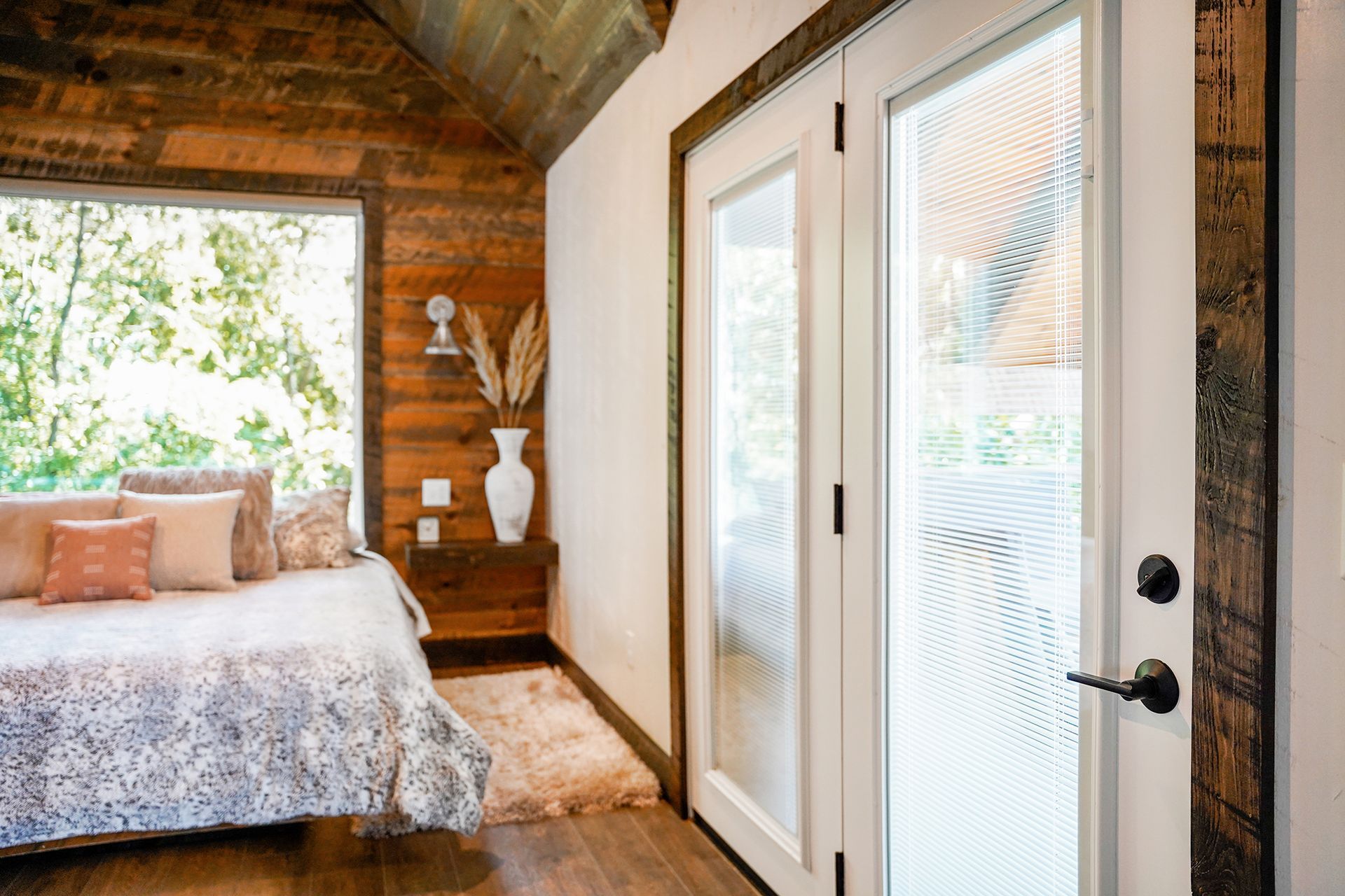 Bedroom with bed near a window, wooden wall, white door, and rug.