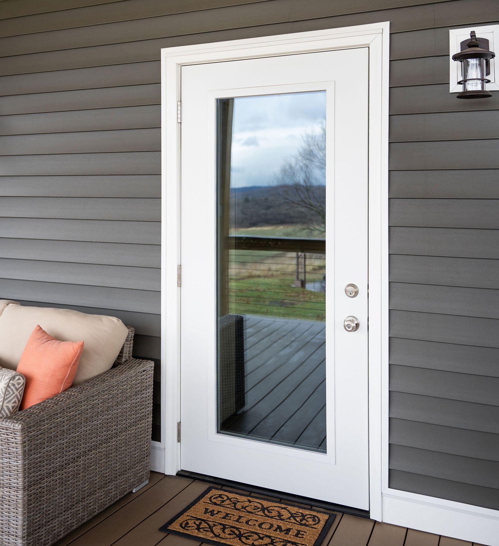 White glass door on a porch, gray siding, wicker couch, welcome mat, mountain view.