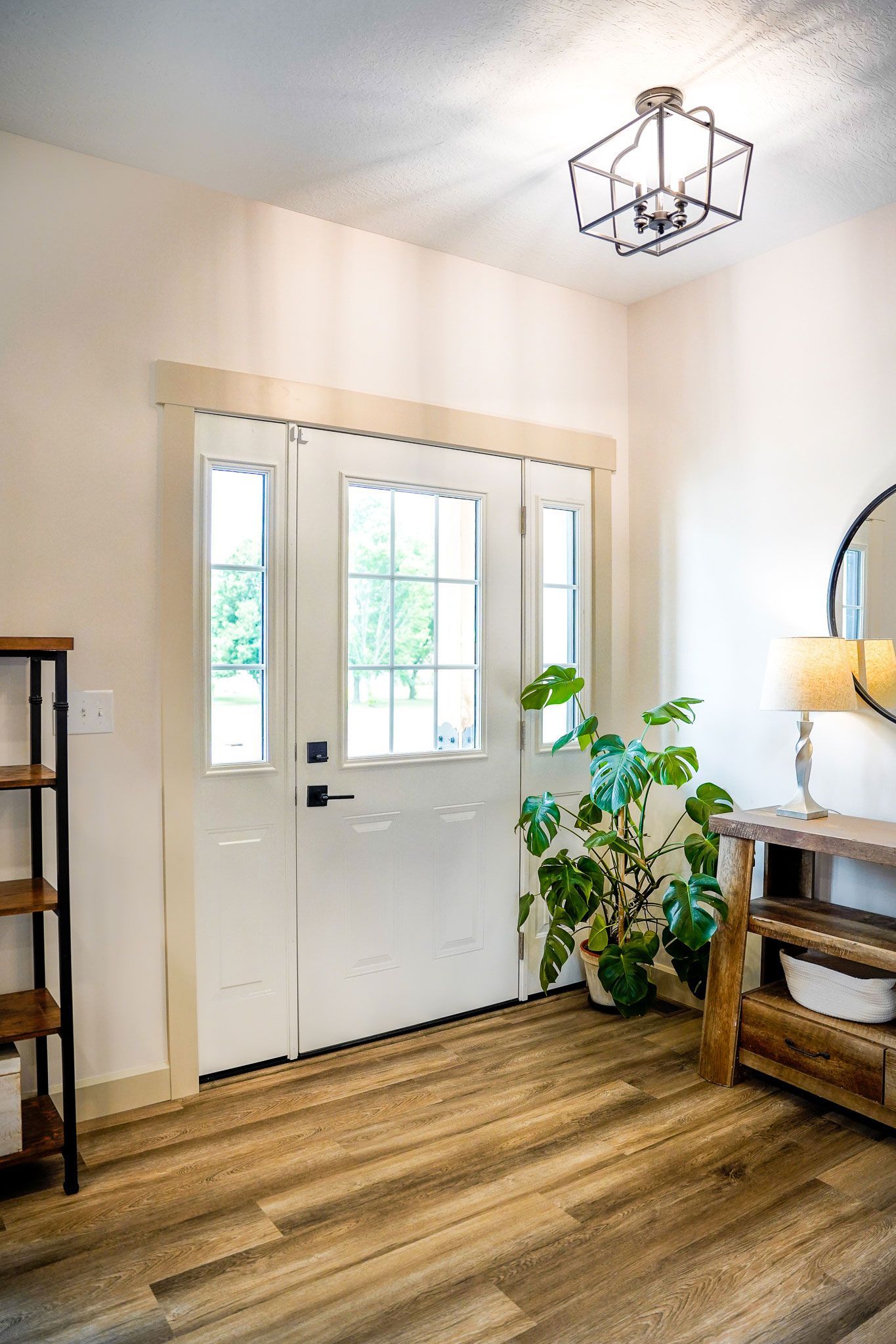 Bright entryway with white door, wood-look floor, and potted plant. Shelf and table on either side.