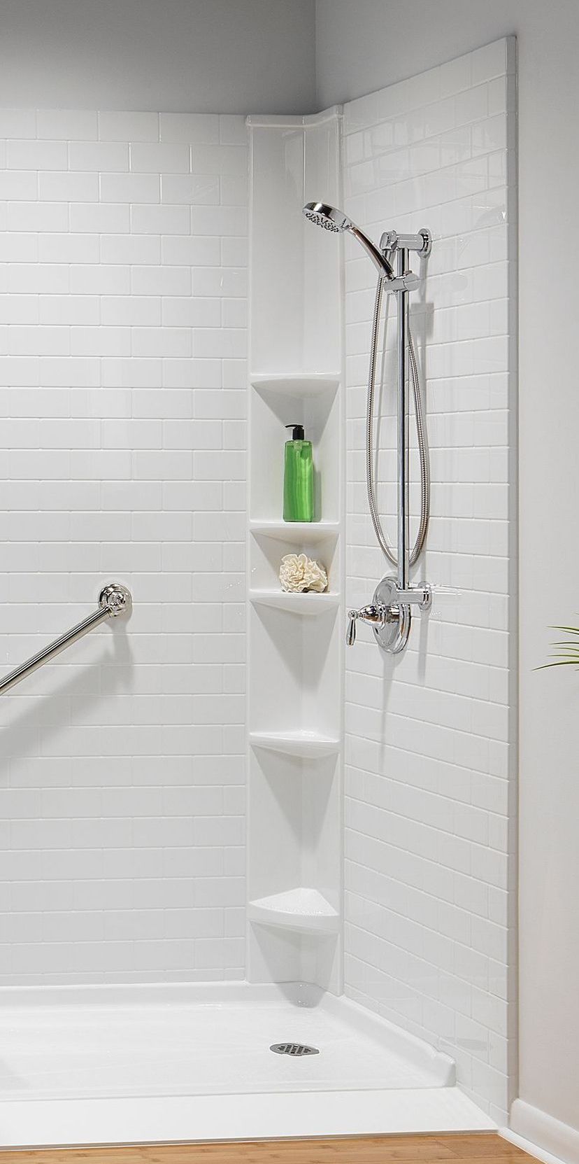 White shower with grab bar, built-in shelves, and showerhead. A bottle of green shampoo sits on a shelf.