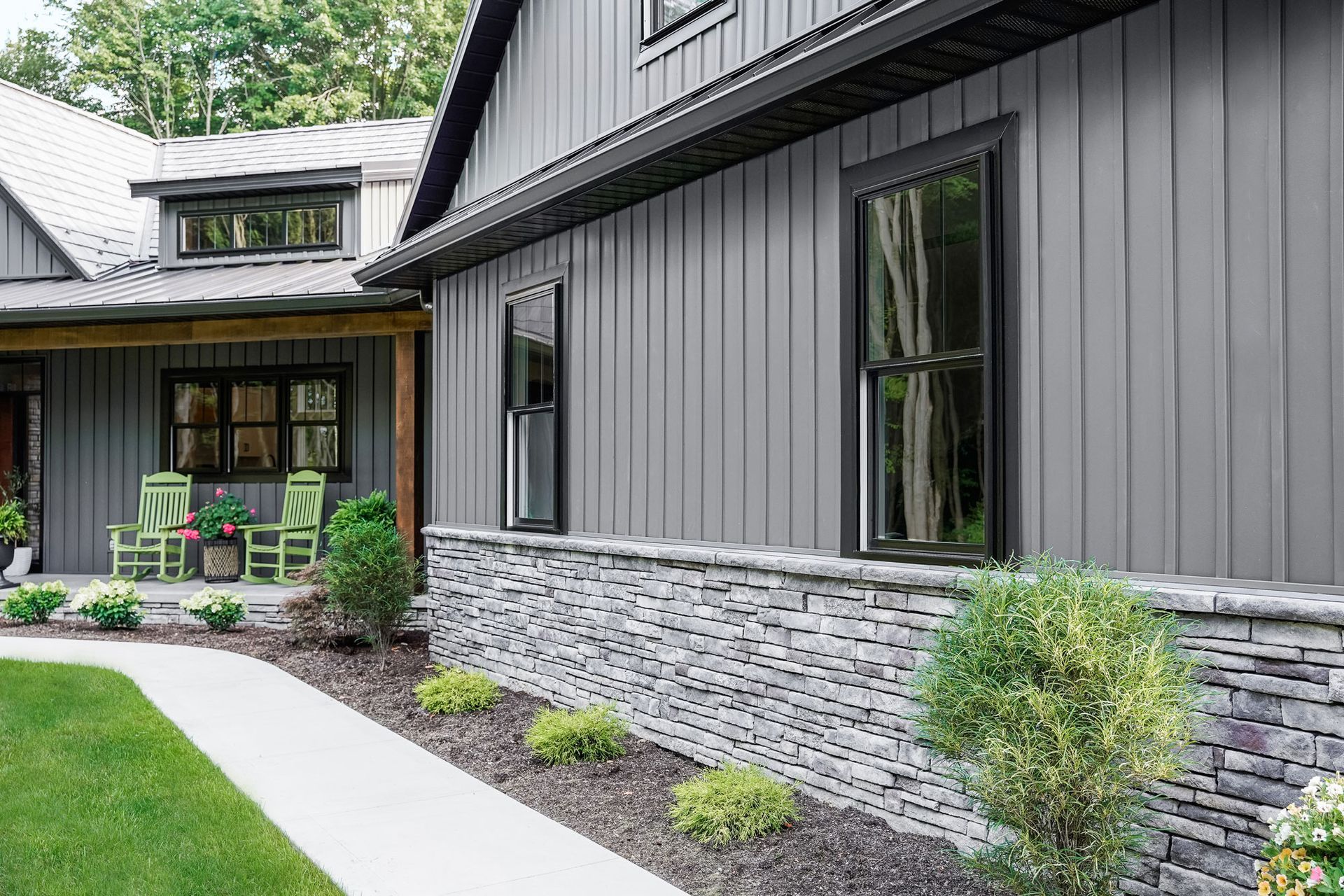 Gray house with vertical siding, stone foundation, and black-framed windows.