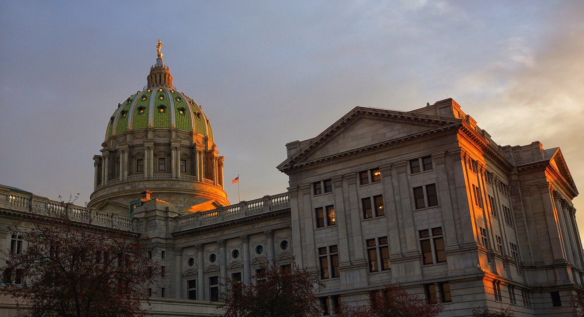 Pennsylvania State Capitol building at sunset, gold sunlight on stone facade and green dome.
