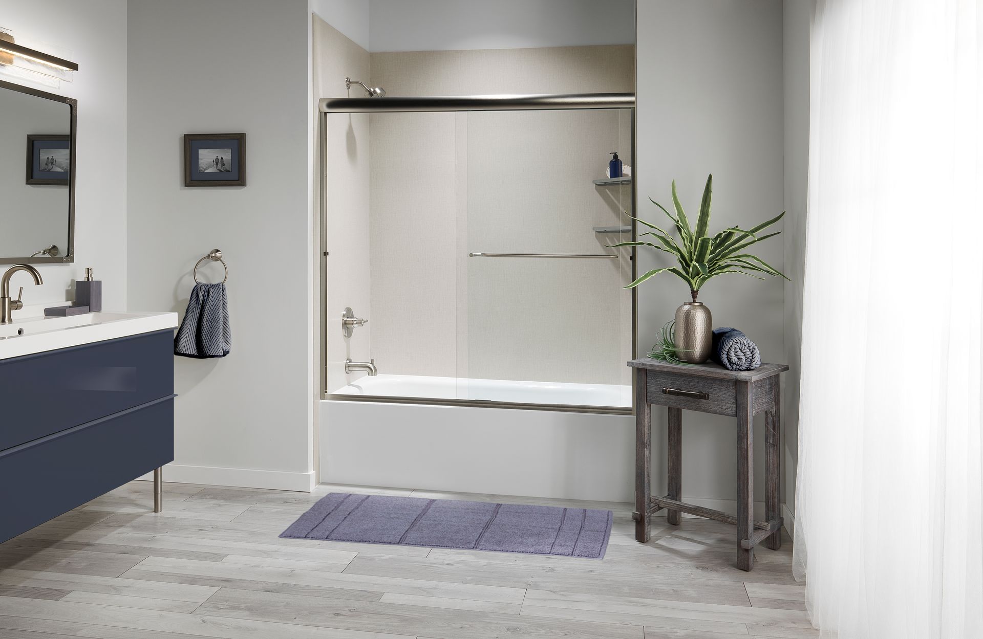 Bathroom with blue vanity, tub with glass doors, rug, and side table.
