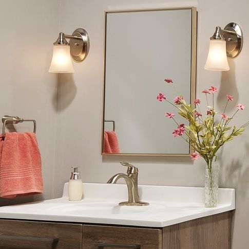 Bathroom vanity with a mirror, sink, towel rack, and lights. Flowers in a vase. Soft lighting.