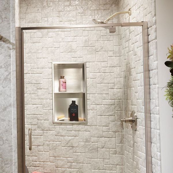 Shower with tiled walls, built-in shelf holding bottles. Glass door, silver fixtures.