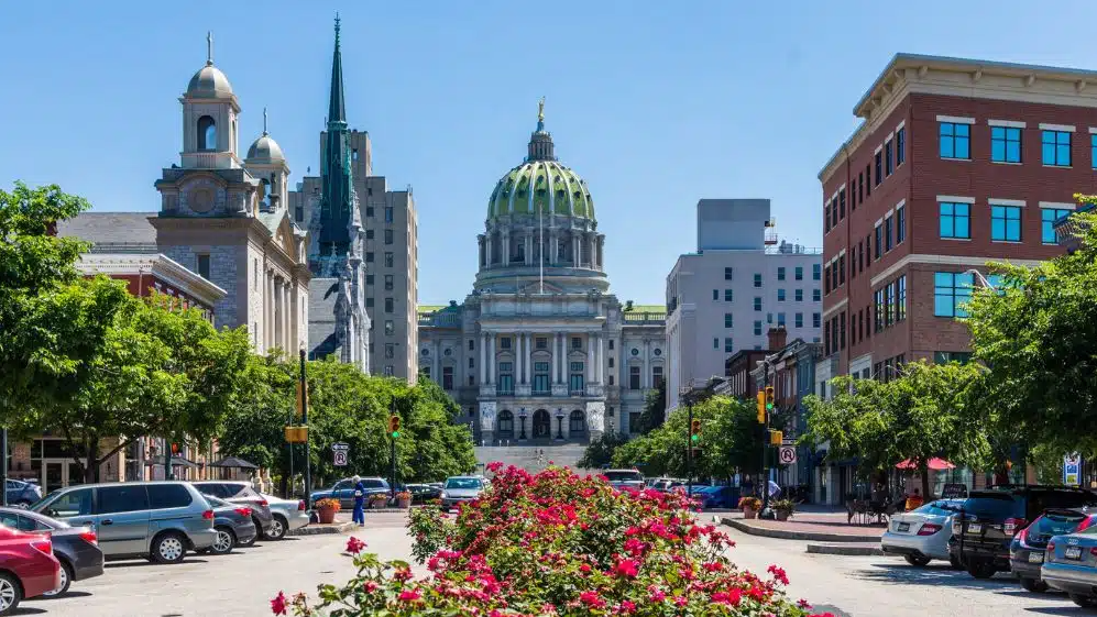 Pennsylvania State Capitol building, Harrisburg, with green dome, ornate facade, and cars on a sunny street.
