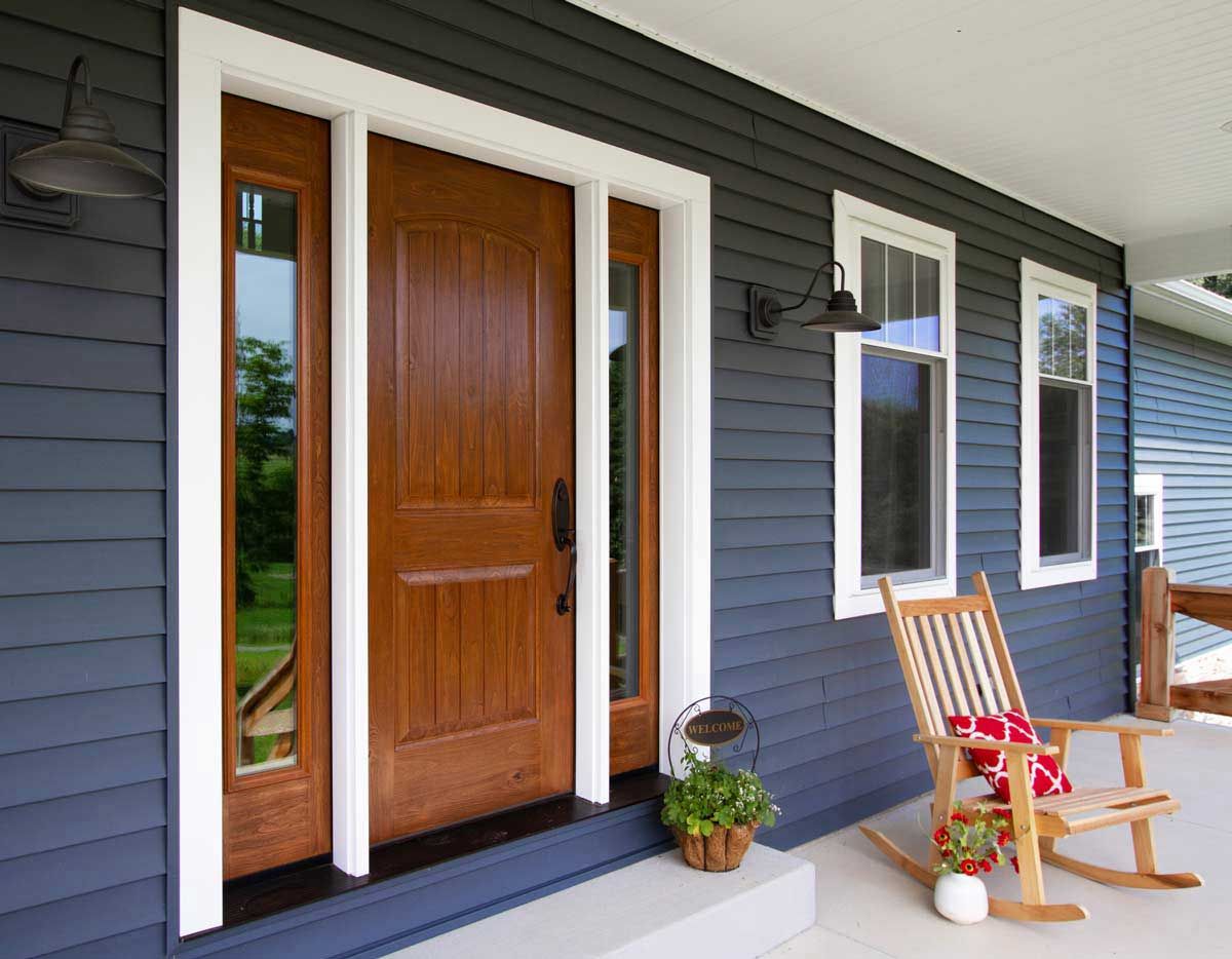 Wooden front door with sidelights, blue siding, rocking chair on porch.