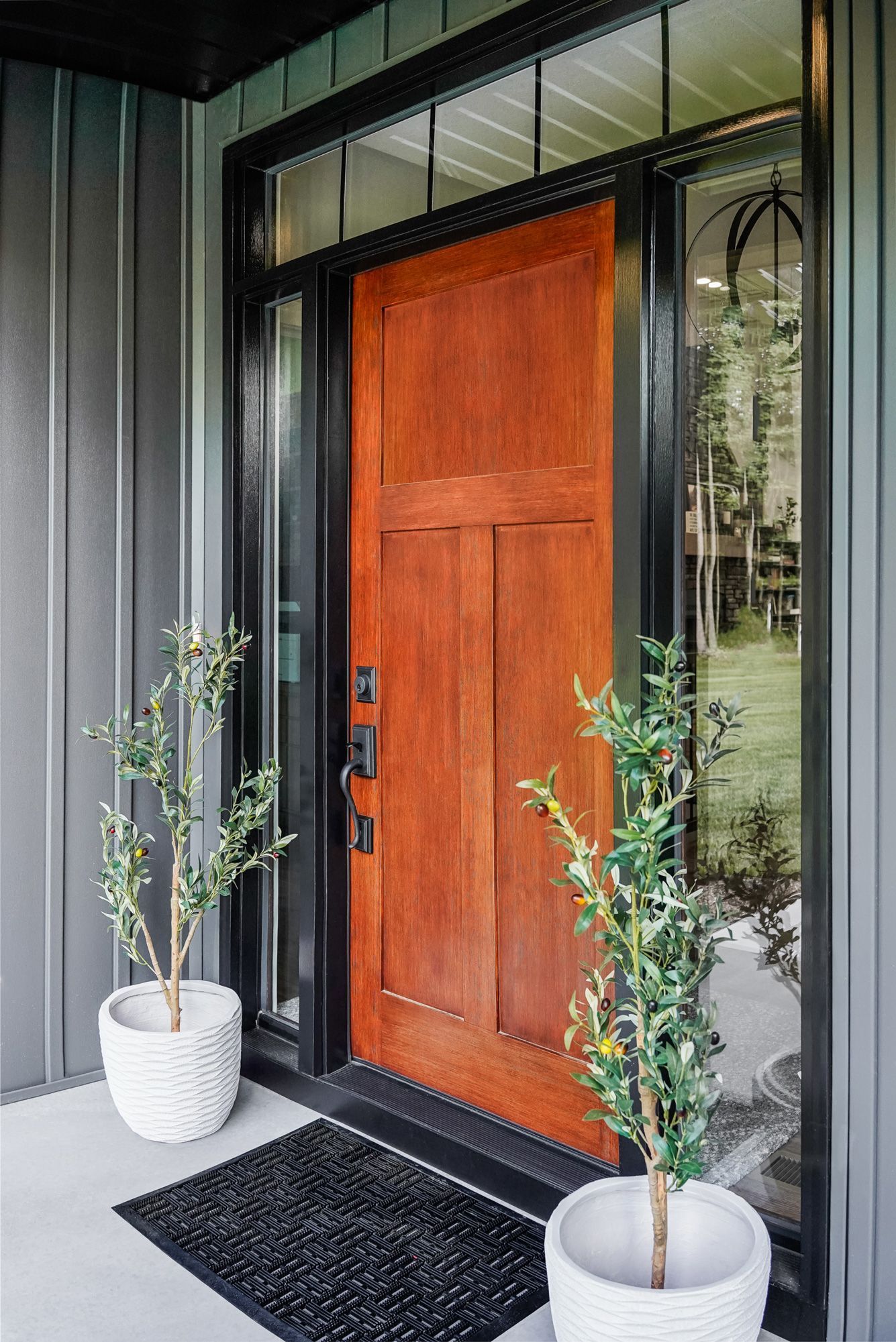 Wooden front door with black trim and two potted plants.
