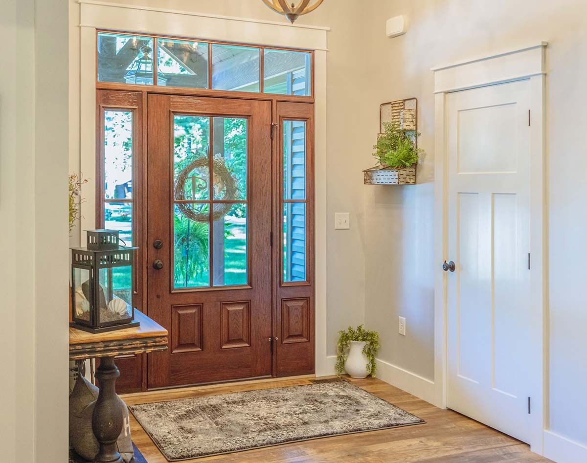 Wooden front door with glass panels and a decorative wreath, entry hallway with neutral walls, rug, and side table.