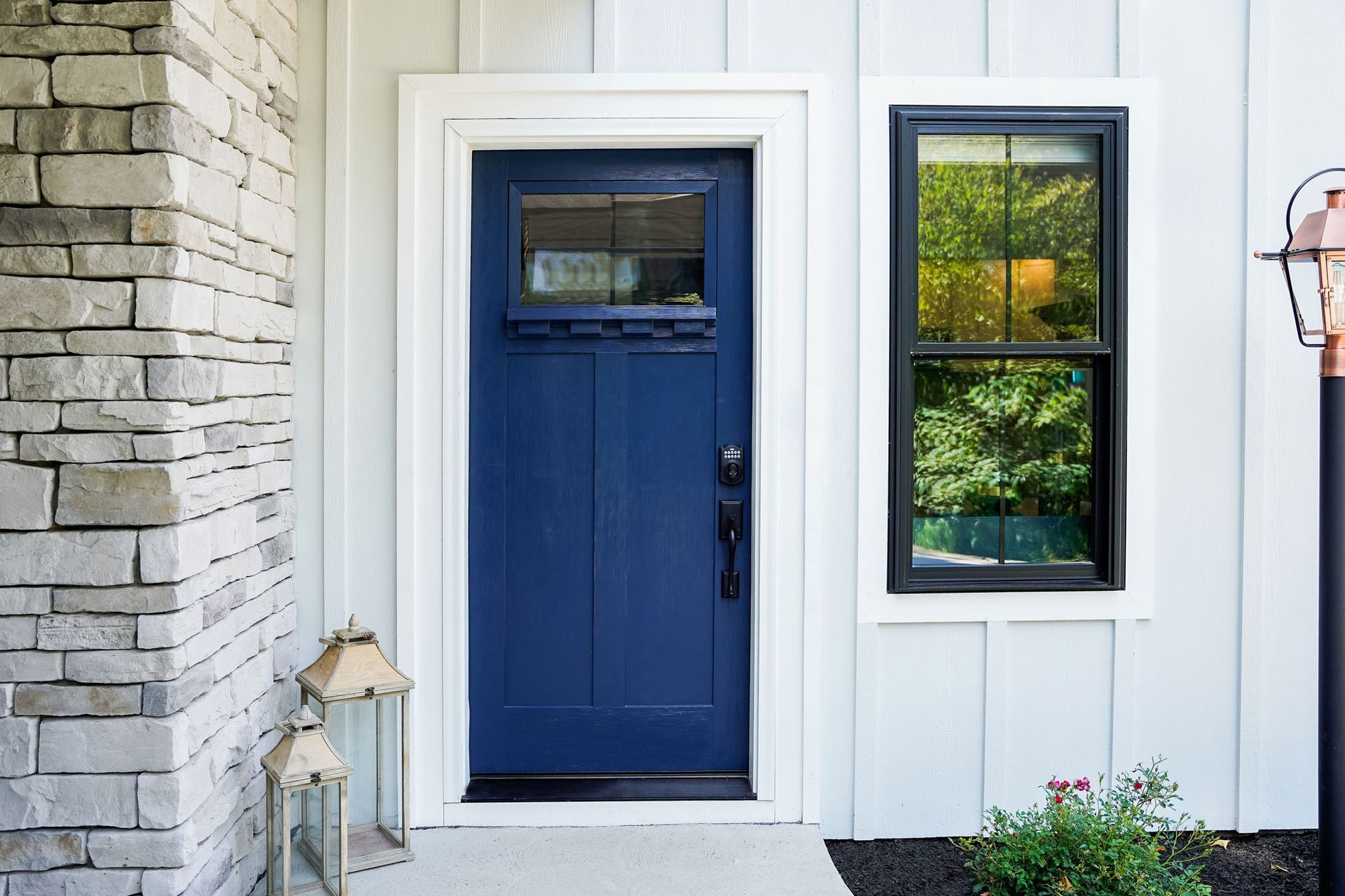 Blue front door with black trim and sidelight. White siding and stone column.