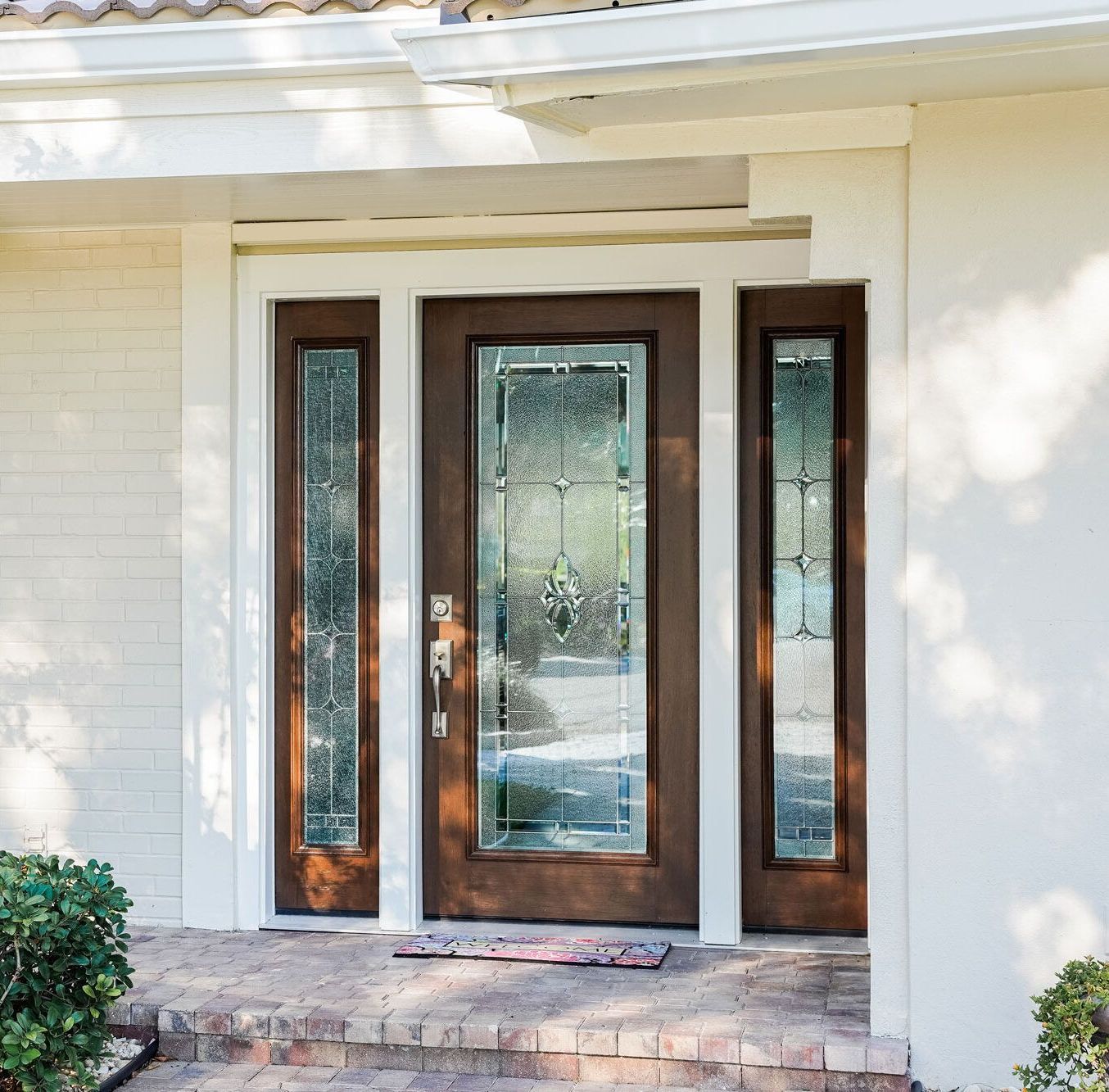 Wooden front door with glass panels and sidelights in a brick entryway.