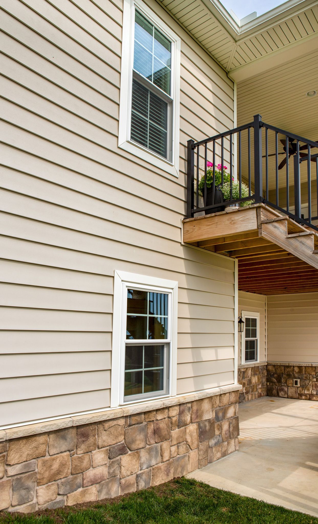 Beige house exterior with windows, stone base, and balcony.
