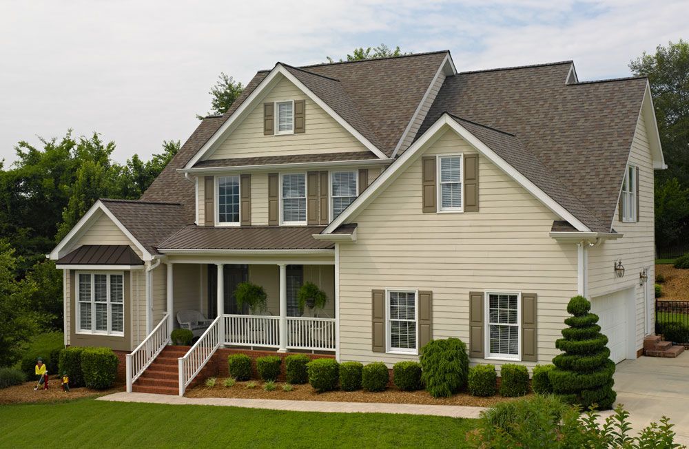 Beige two-story house with brown roof, green lawn, white porch, and matching shutters.