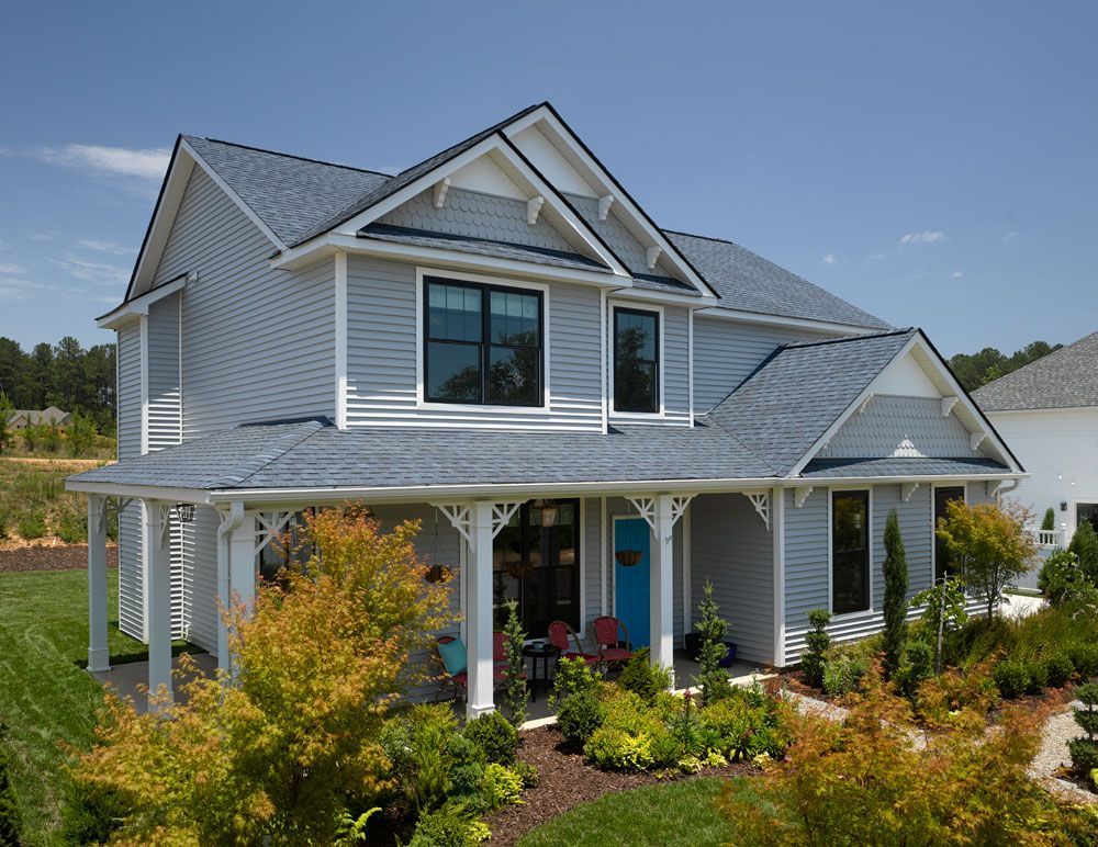 Two-story blue house with white trim, porch, and landscaping under a blue sky.