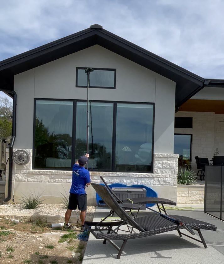 Person on patio beside house, near lounge chairs and large windows.