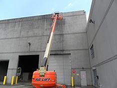 Orange JLG lift extended to clean a tall, gray concrete building exterior.