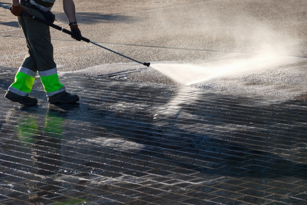 Technician using high-pressure washer on brick building