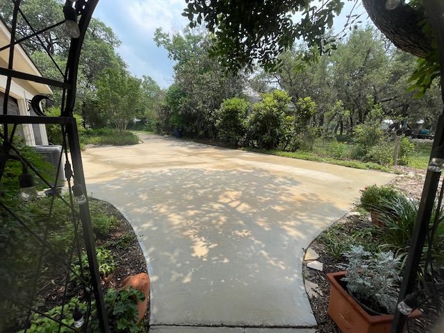 A concrete driveway leading to a house surrounded by trees and bushes.
