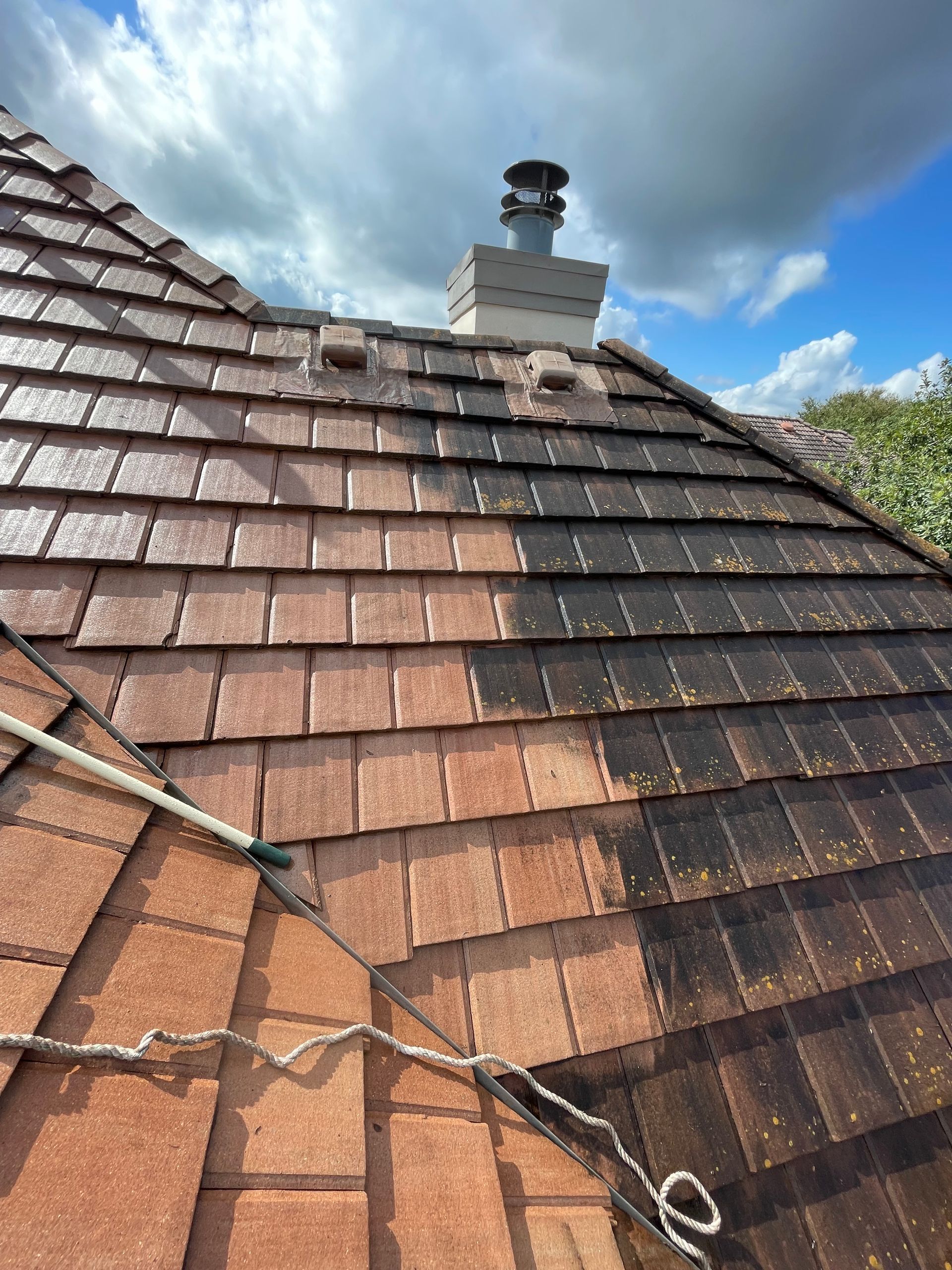 Tiled roof with visible wear and a chimney under a cloudy sky
