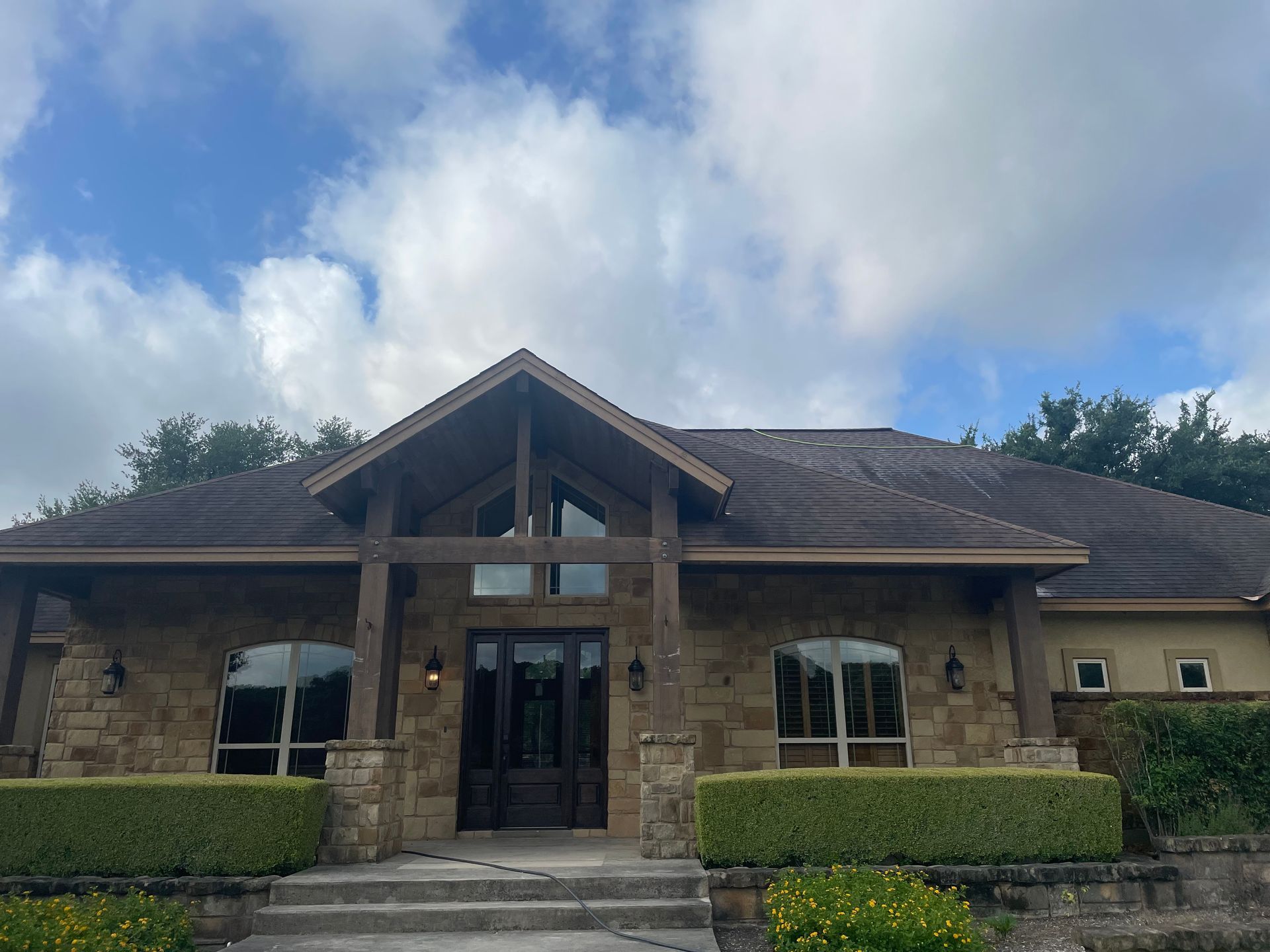 Stone building entrance with peaked roof, glass doors, and trimmed hedges under a cloudy sky
