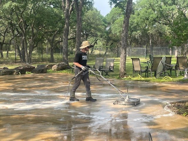 Person pressure washing a concrete patio outdoors with trees in the background in Spring Branch