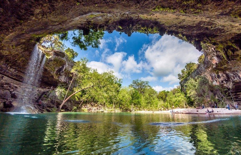 A waterfall is coming down a cliff into a lake surrounded by trees.