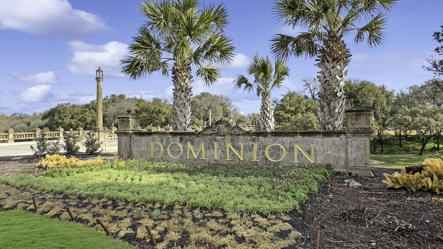 A sign for dominion is surrounded by palm trees and grass.