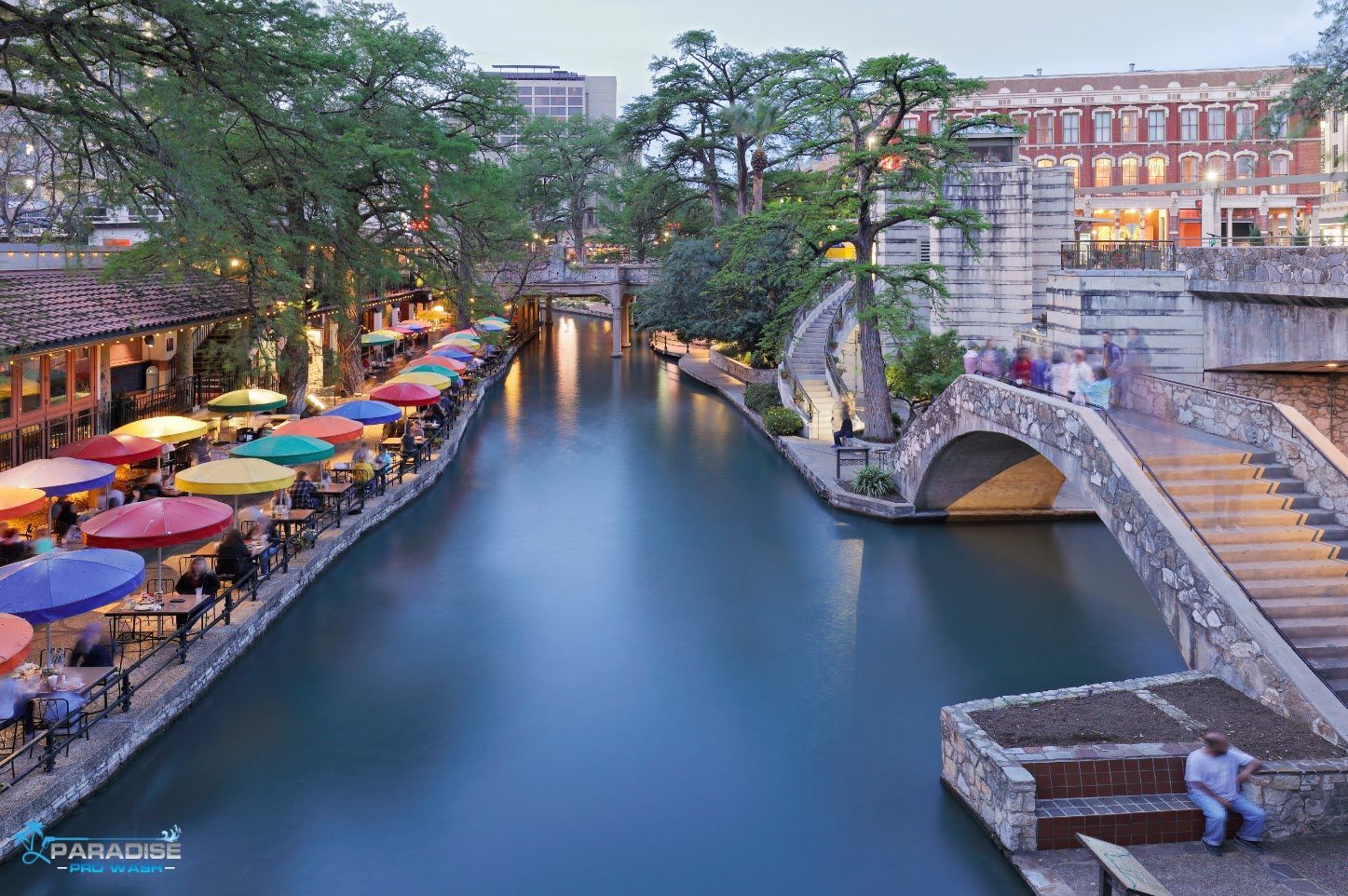 A river with a bridge and umbrellas on the side of it.
