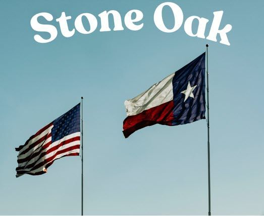 Two flags are flying in front of a sign that says stone oak
