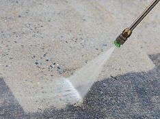 A person is using a high pressure washer to clean a concrete floor.