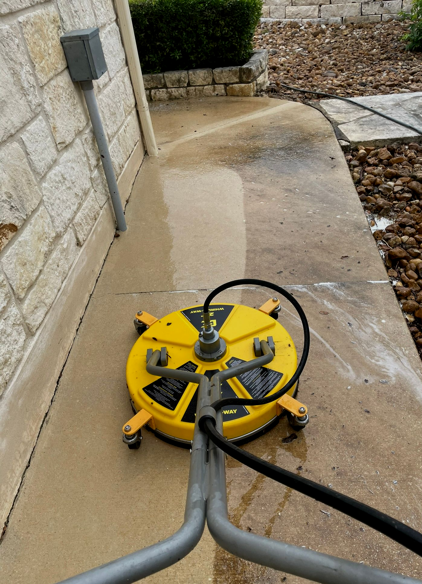 Yellow pressure washer hose reel on a wet concrete patio beside a stone wall