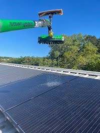 A green brush is cleaning a solar panel on a roof.