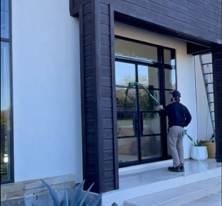 Person opening black-framed glass doors of a modern home with dark wood siding