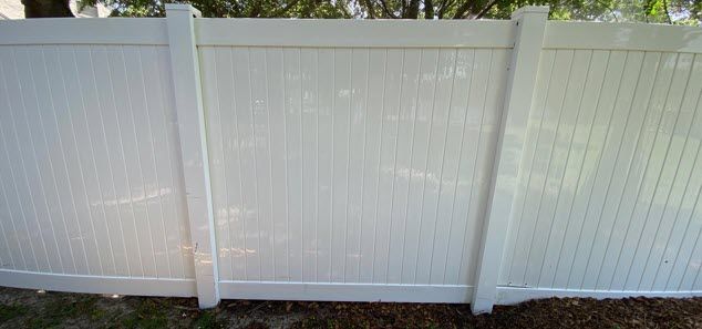 A white vinyl fence is sitting in the grass next to a tree.