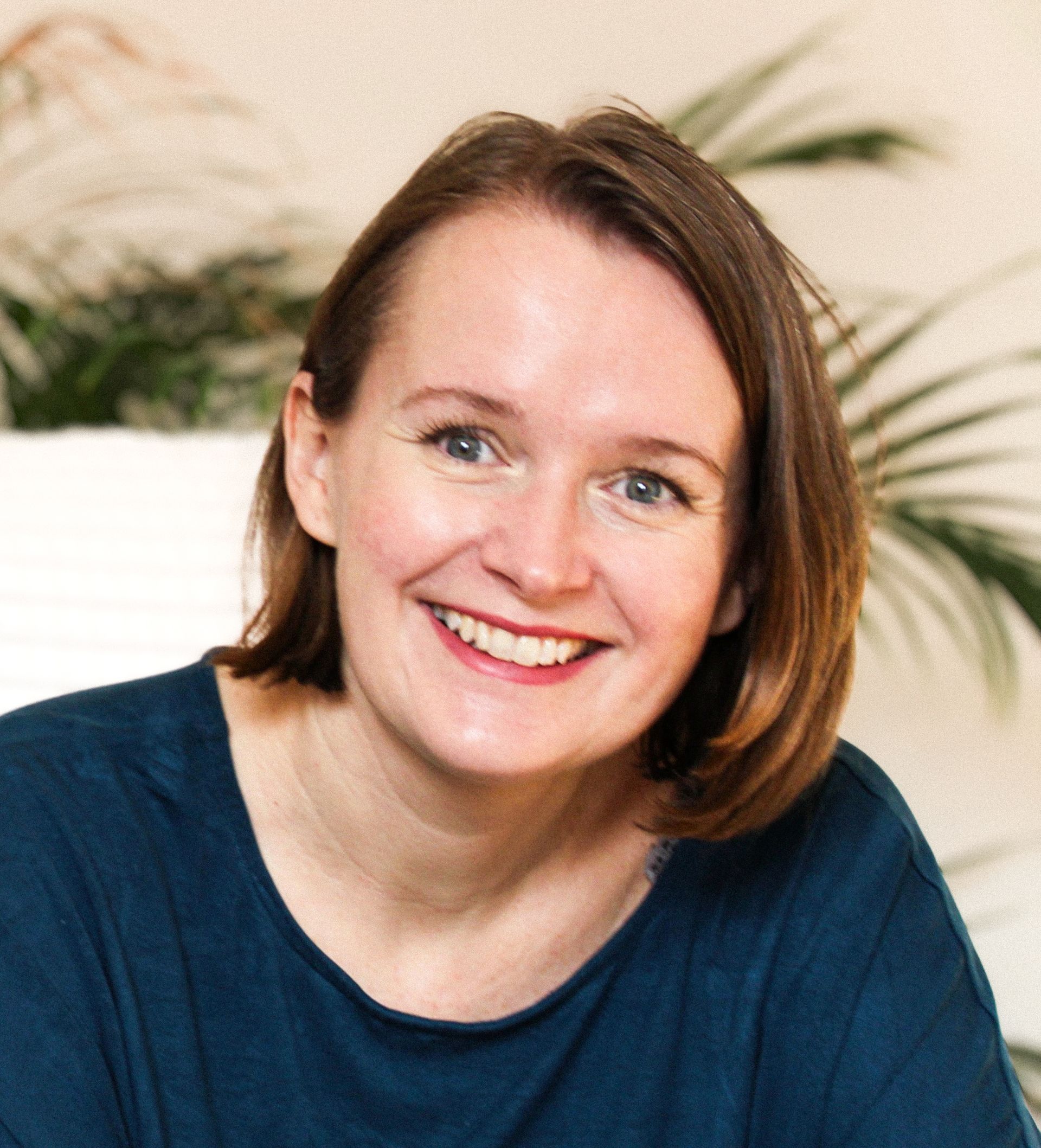 Portrait von Tina Schwarzfischer mit einem freundlichen Lächeln vor einem weichen, blattreichen Hintergrund.