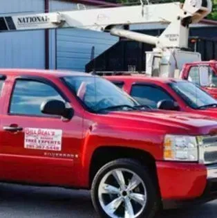 Red pickup truck with company decals parked beside another red truck near a building and utility equipment