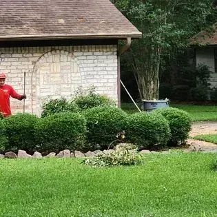 Person in red jacket near a white stone house, with green bushes and lawn in the foreground.