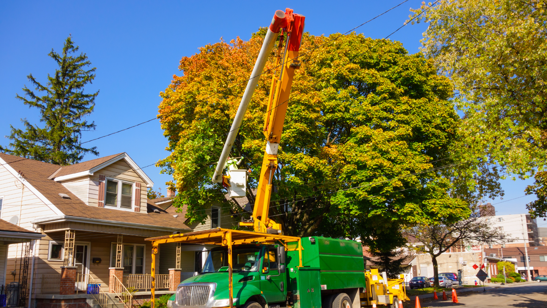 Tree removal truck with raised boom beside a house on a sunny residential street