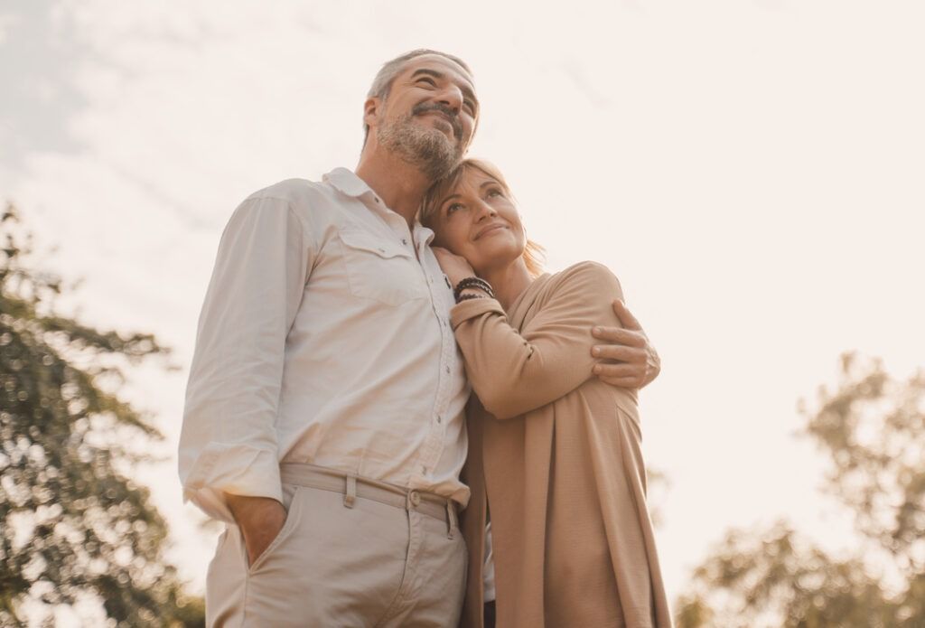 Two people standing outdoors, leaning close together in soft warm light