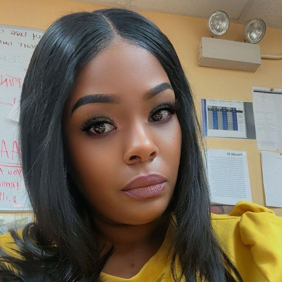 Woman in a yellow top posing indoors with a neutral expression, office wall behind her.