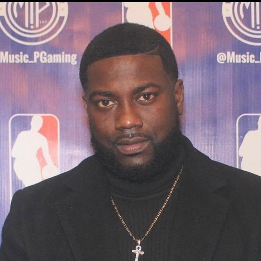 Man in black turtleneck and chain posing at a purple step-and-repeat backdrop
