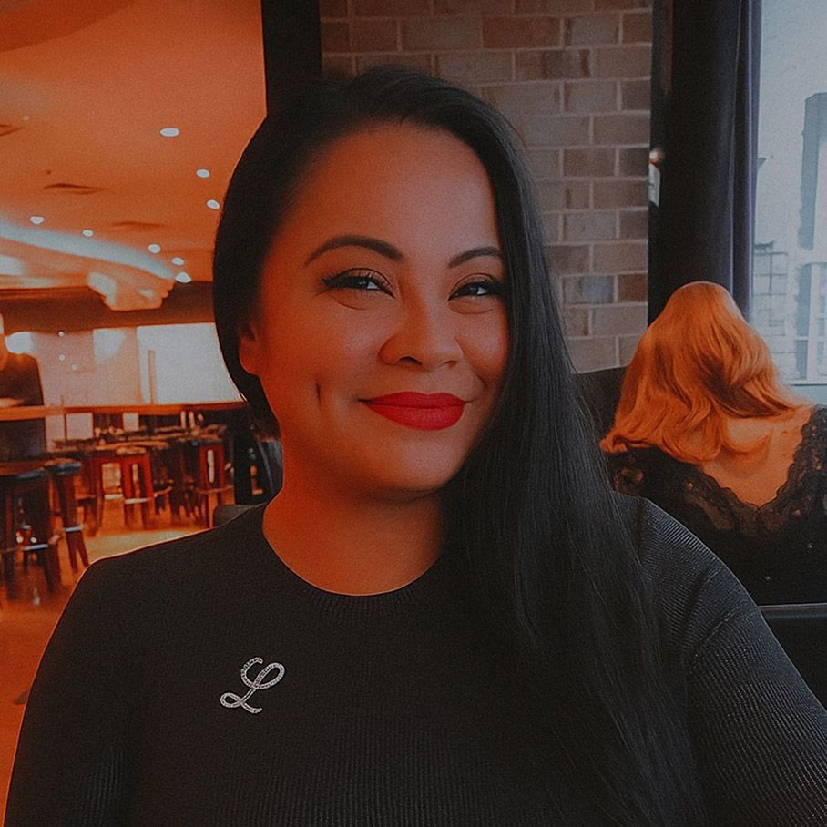 Smiling woman in a black top seated in a warm-lit café with orange walls and brick accents