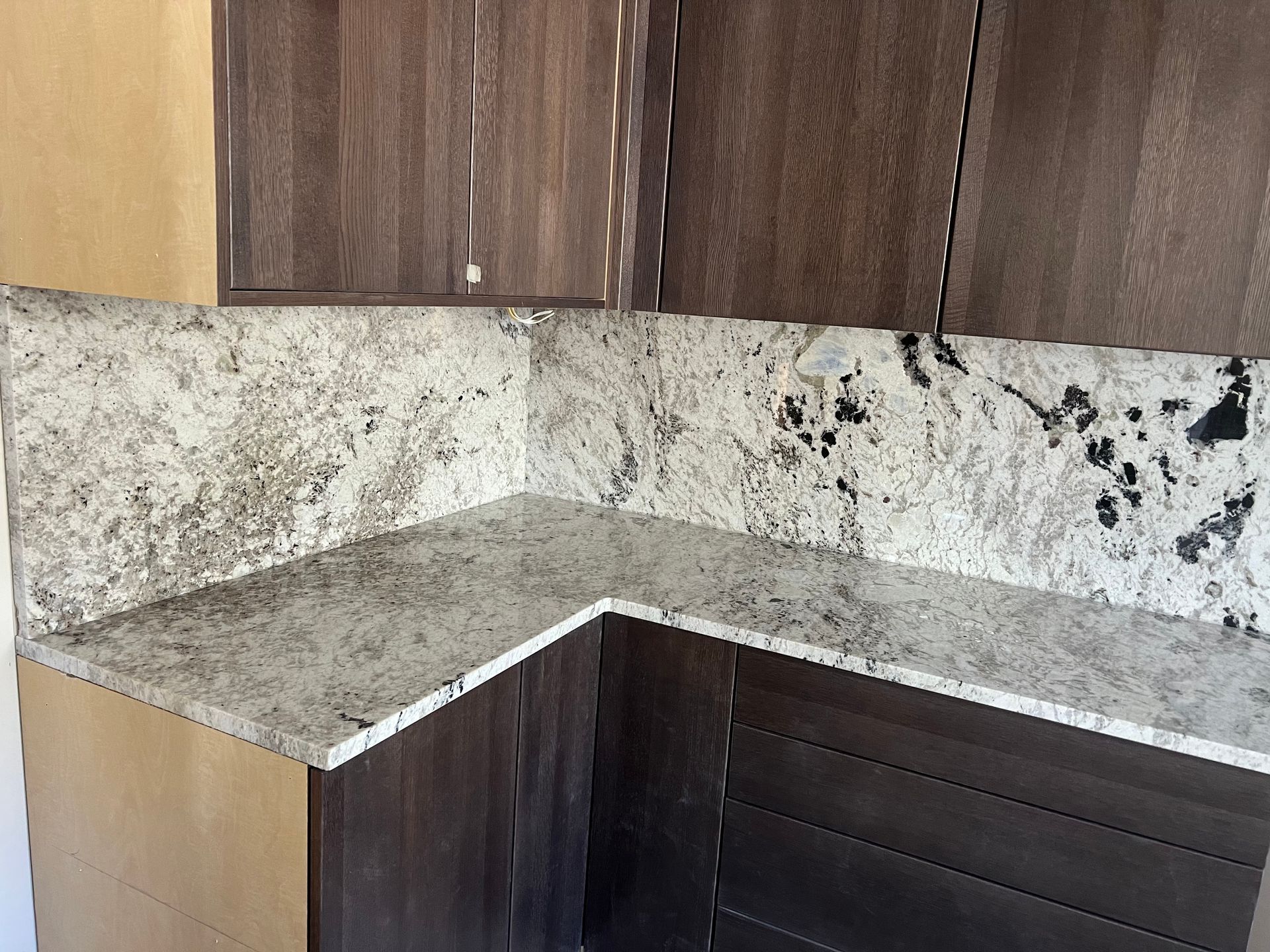 Corner kitchen countertop with gray granite backsplash and dark wood cabinets
