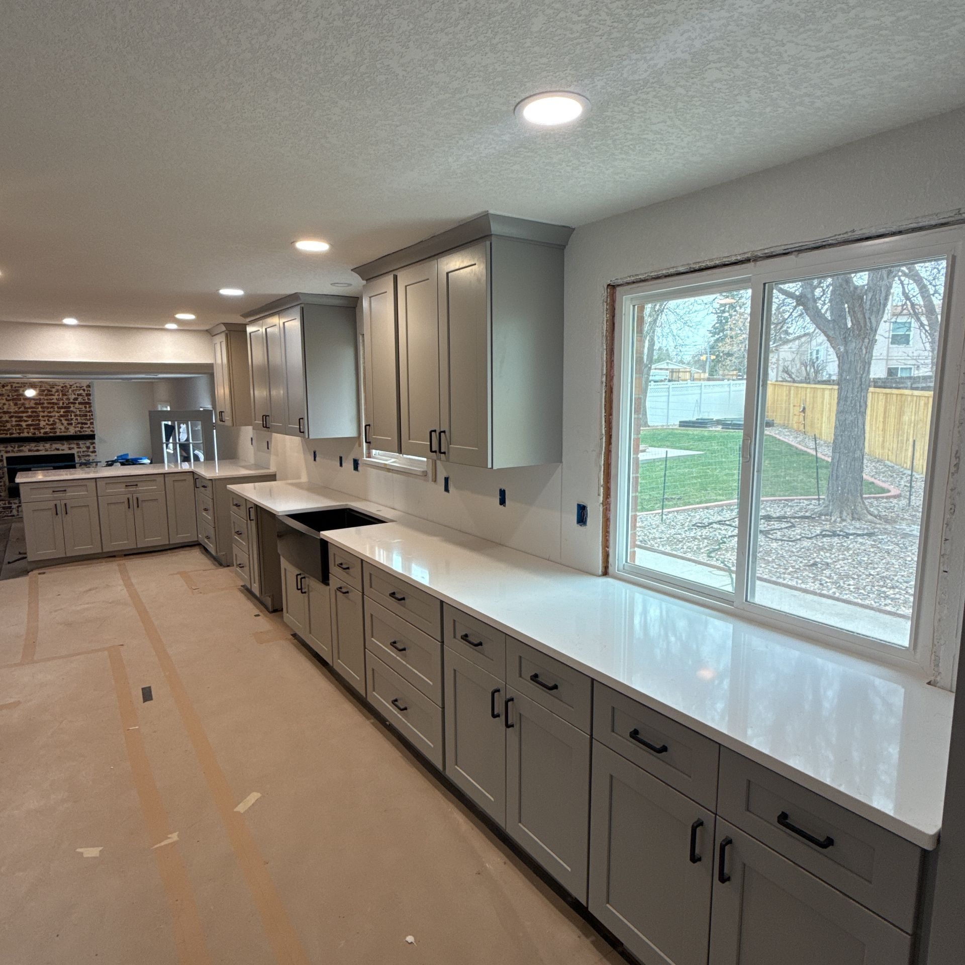 Bright modern kitchen with gray cabinets, white countertop, and large window overlooking a yard
