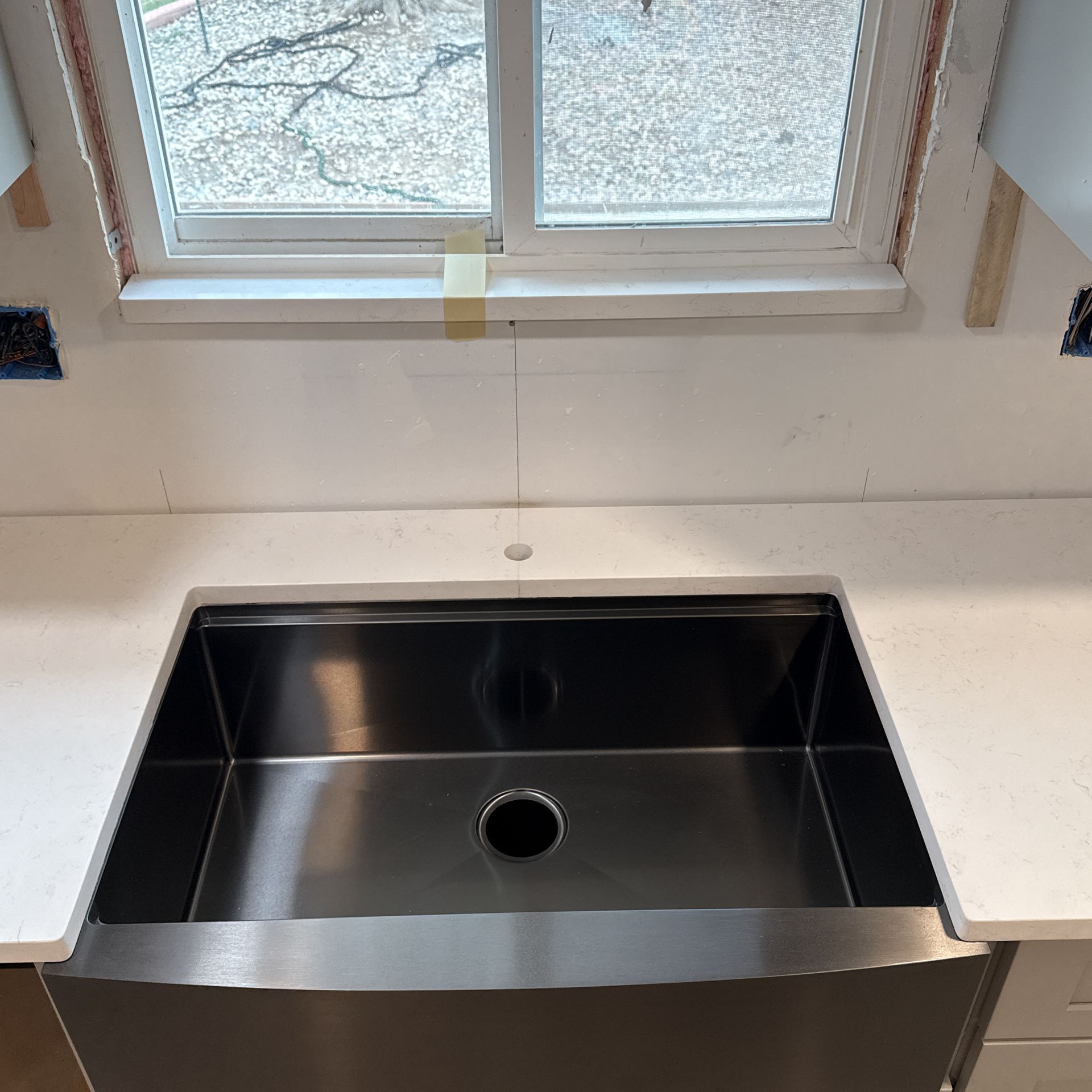 Stainless steel kitchen sink beneath a window with white countertop and backsplash.