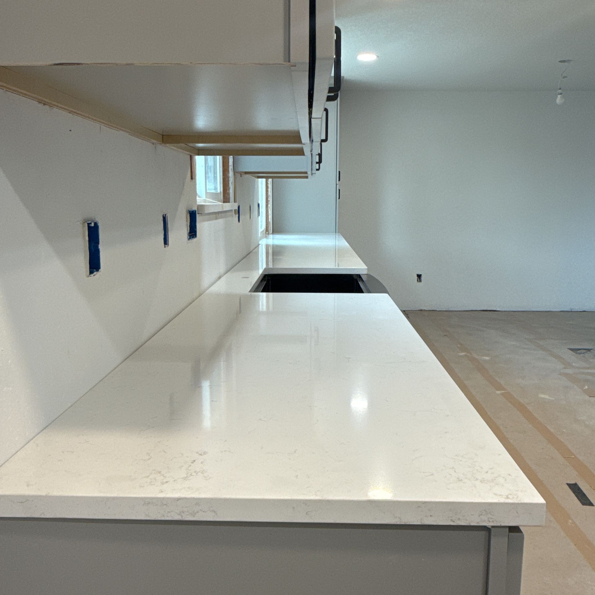 Empty modern kitchen with white countertops and unfinished flooring in a bright room