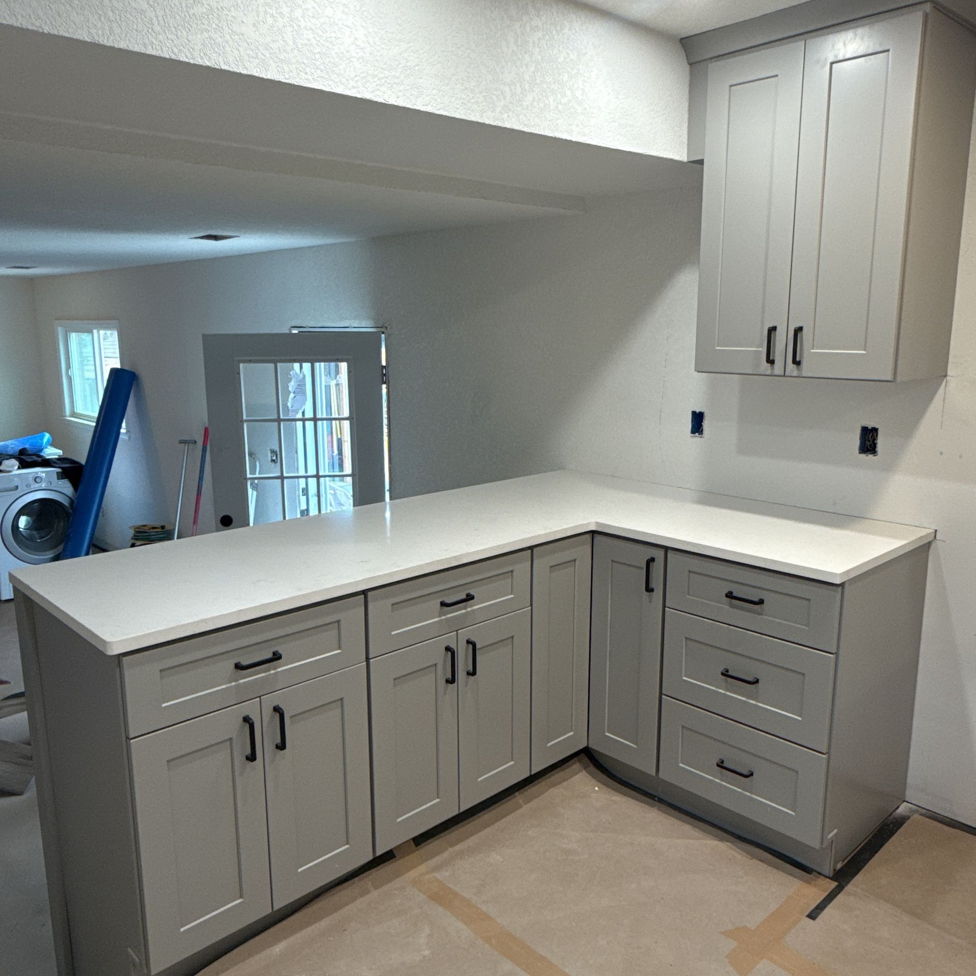 Gray kitchen cabinets and white countertop in an unfinished room with a pass-through opening and open floor space