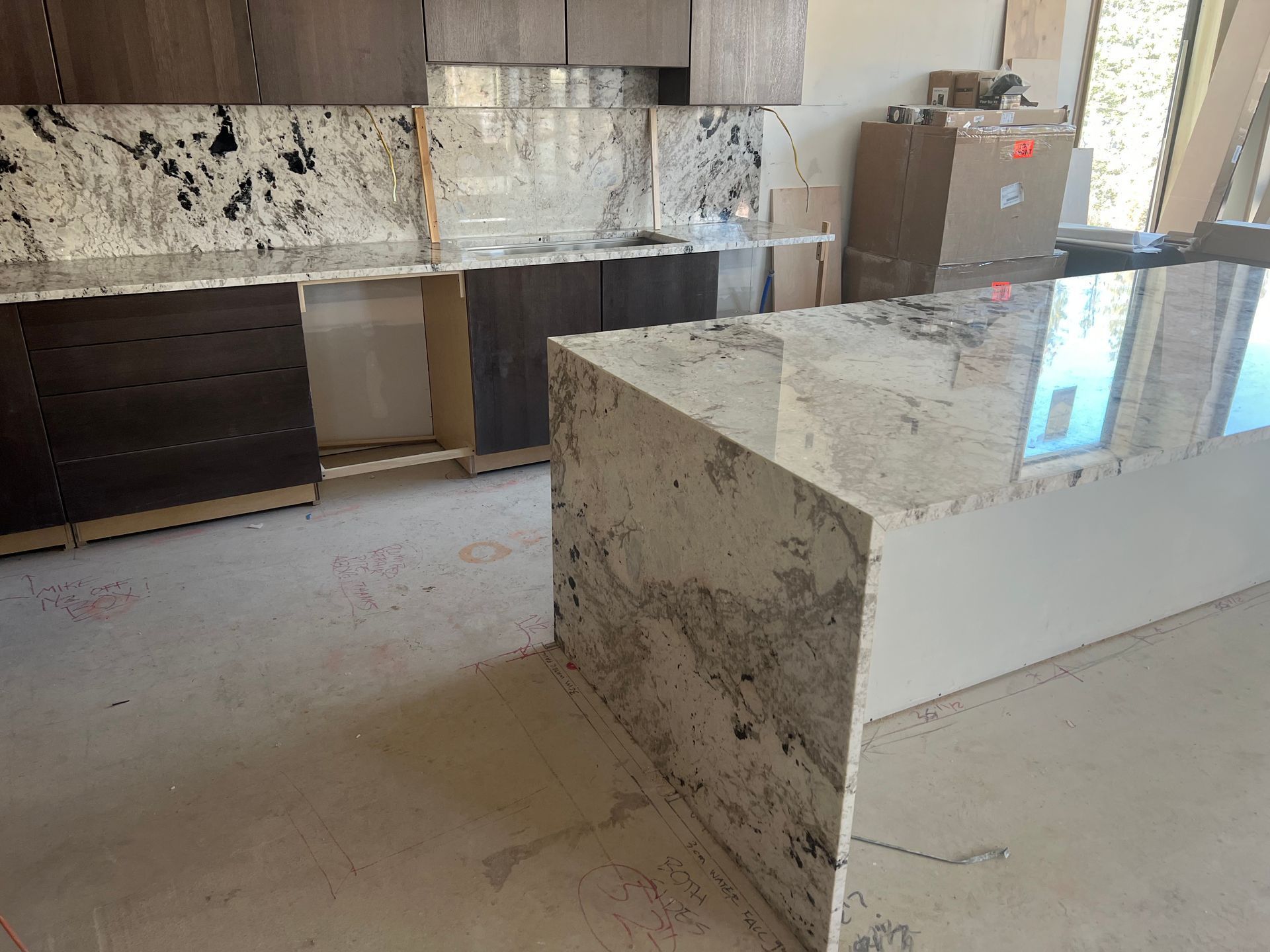 Modern kitchen with marble countertops, dark wood cabinets, and a central island under renovation.