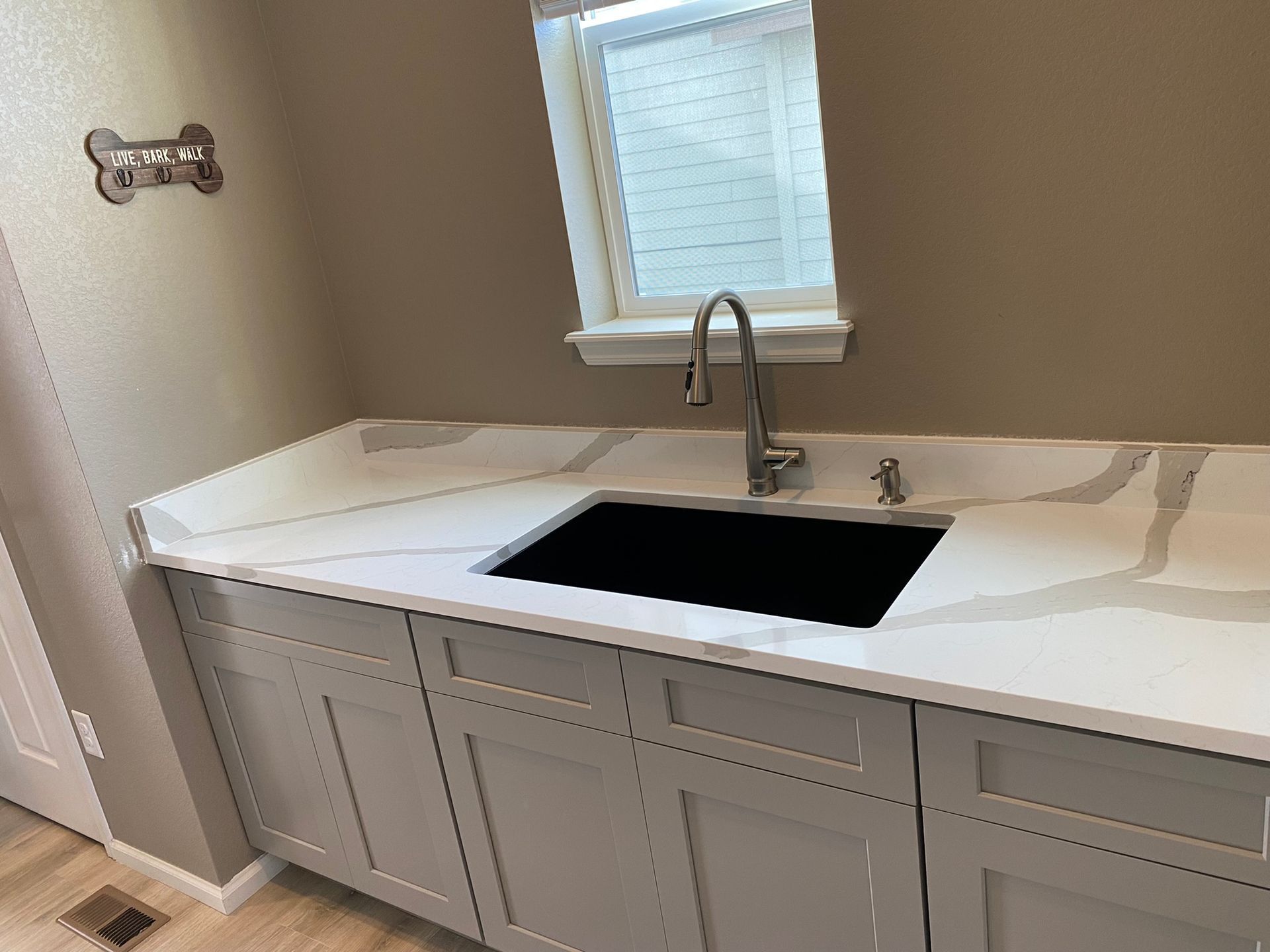 Bathroom vanity with white countertop, black sink, and chrome faucet under a window