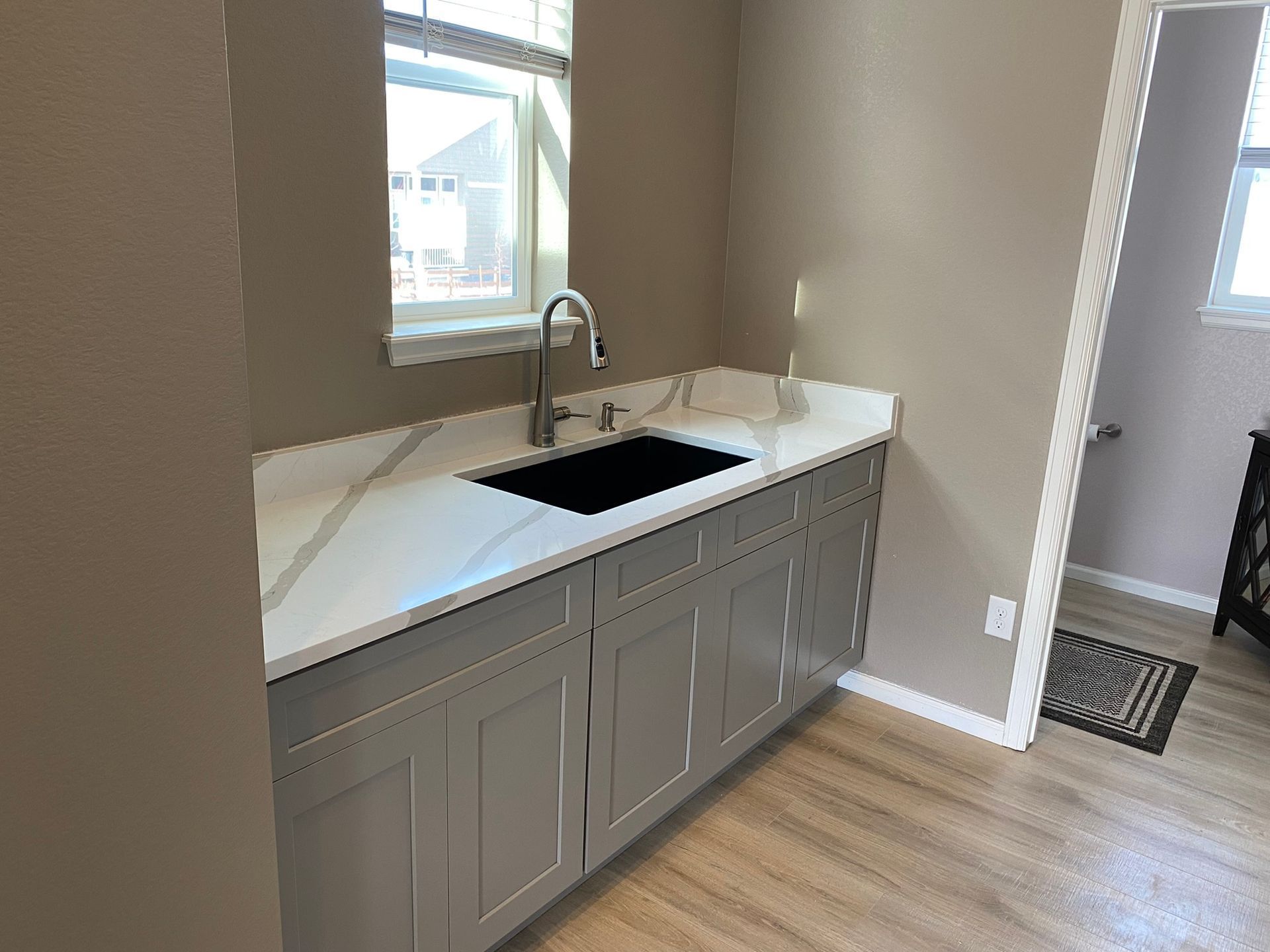 Modern kitchen with gray cabinets, white countertop, black sink, and window above the sink.